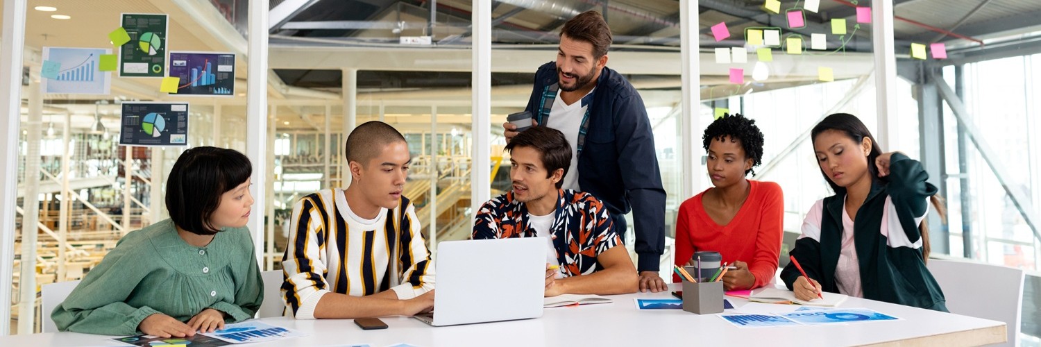 Sechs Personen am Schreibtisch arbeiten zusammen an Unterlagen und Laptop